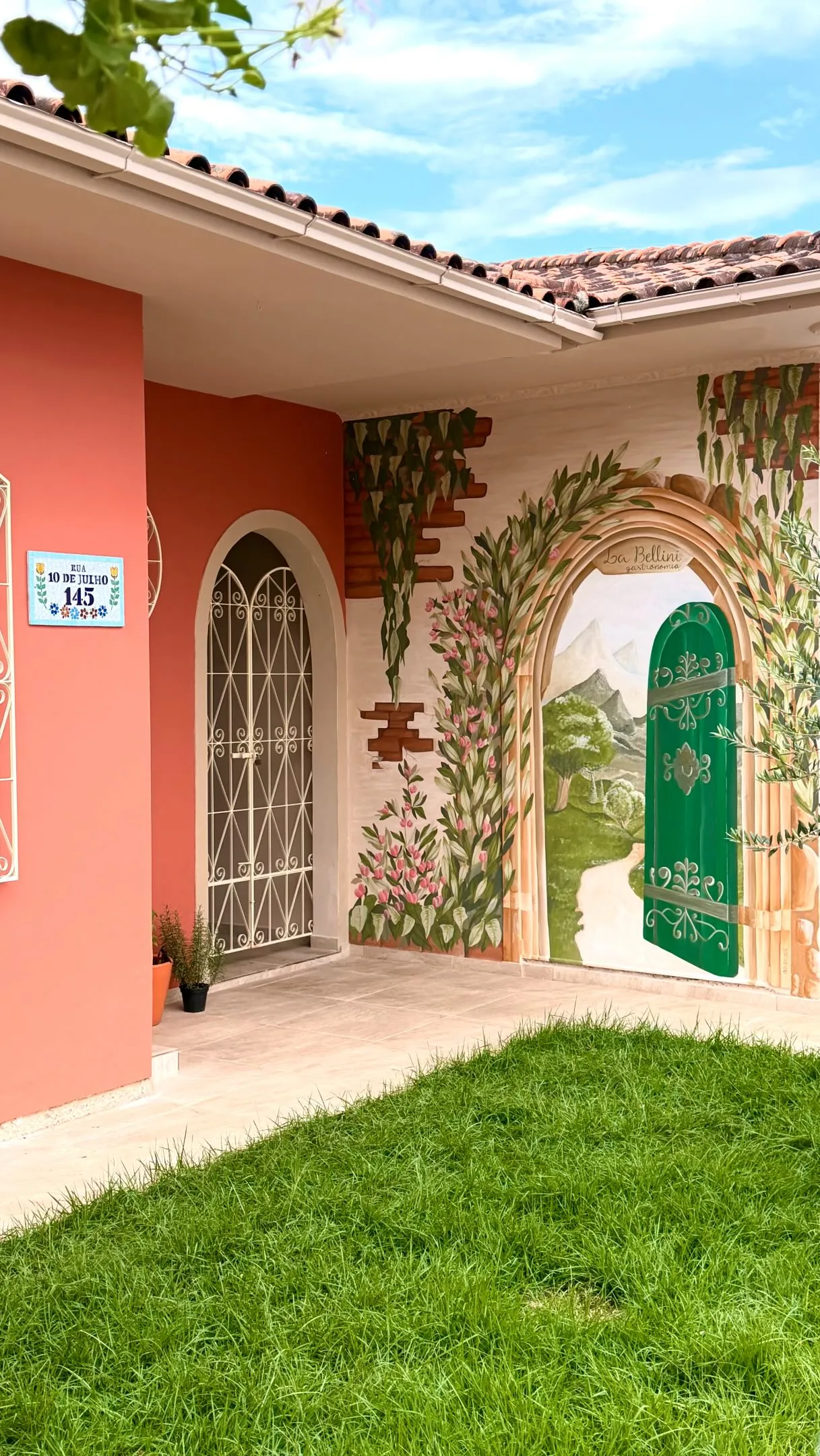 Fachada rosa-coral da Casa La Bellini, com mural pintado à mão e porta verde